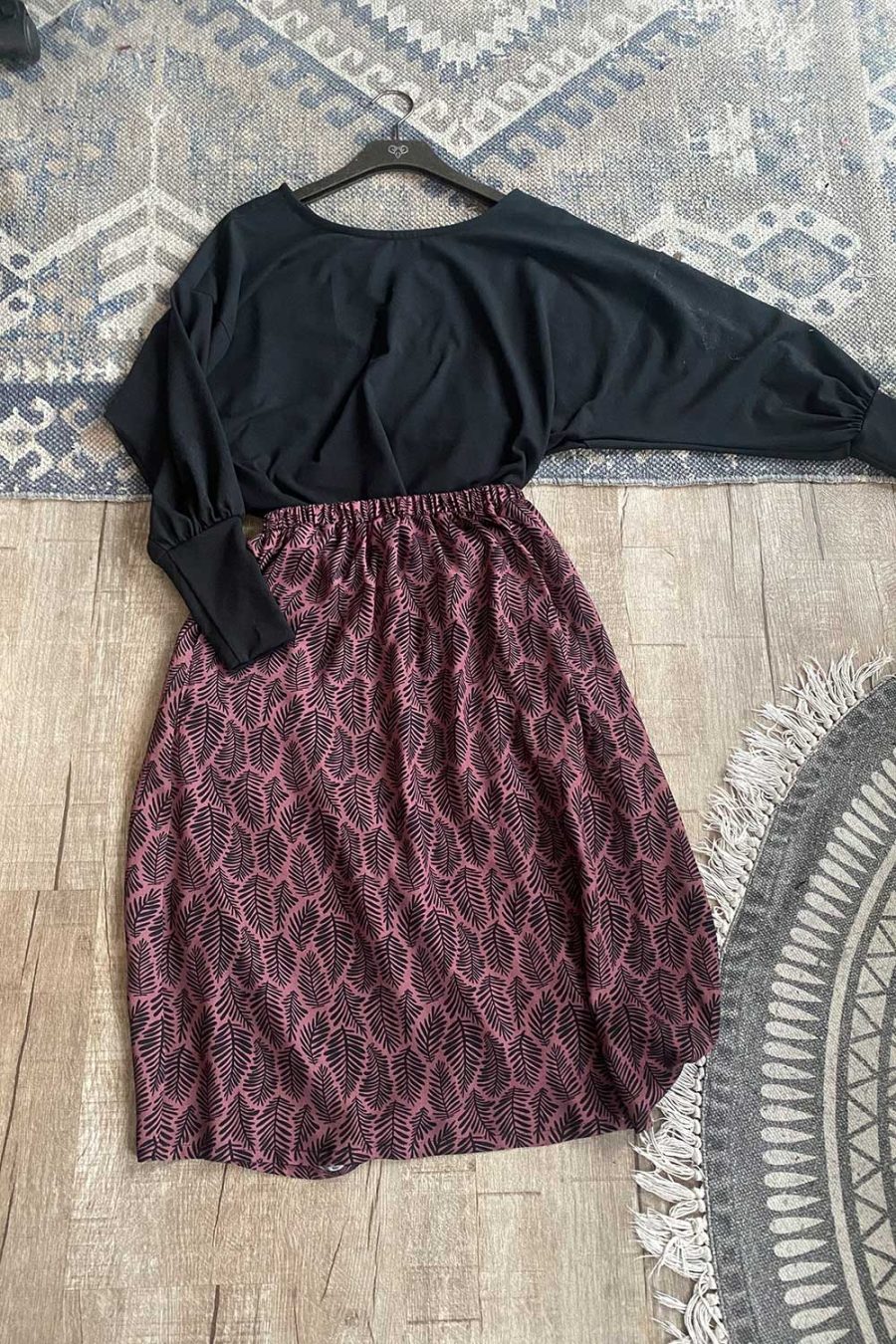 Outfit: Shirt AVA schwarz aus Bio-Baumwolle und Rock SYMPLA in Beere mit schwarzem Blattmuster aus ECOVERO® – knielanger, nachhaltiger Damenrock mit elastischem Bund und Taschen.